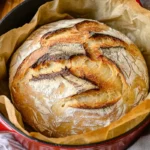 Freshly baked sourdough discard bread in a Dutch oven with a golden, cracked crust.