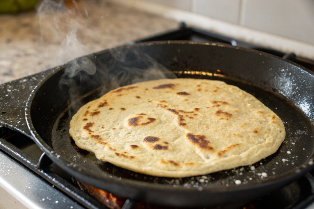 A puffed sourdough discard tortilla cooking on a hot cast-iron skillet with golden brown spots and steam rising.