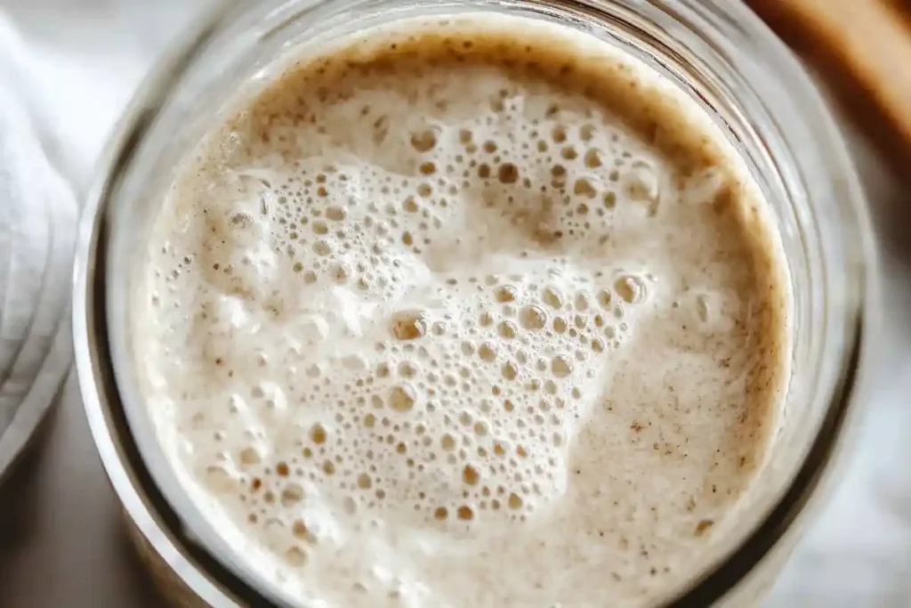 A close-up view of bubbly and active sourdough starter in a clear jar, showcasing its texture and readiness for baking.