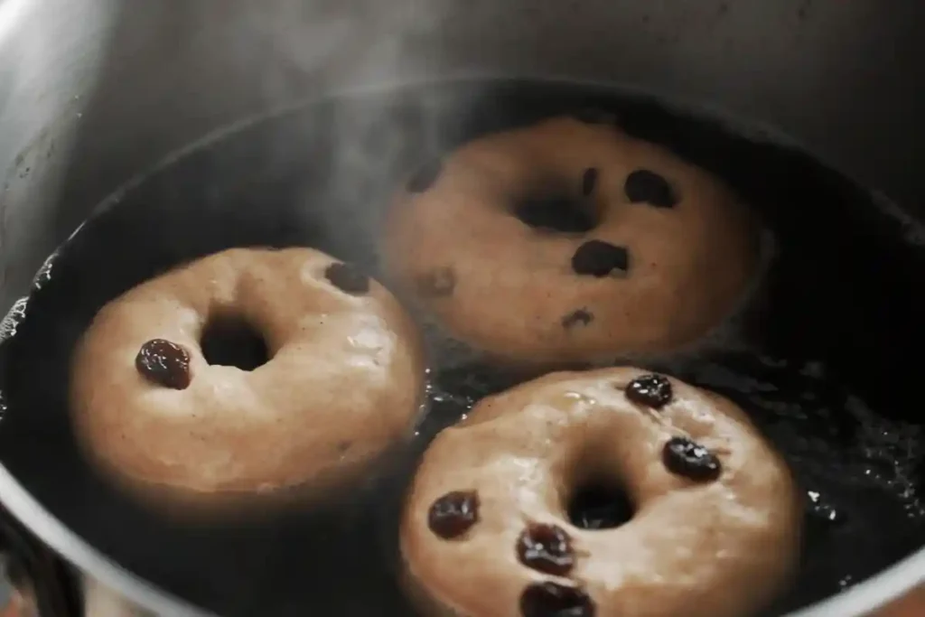 Three sourdough cinnamon raisin bagels boiling in a pot of water, creating a steamy effect for chewy bagel texture