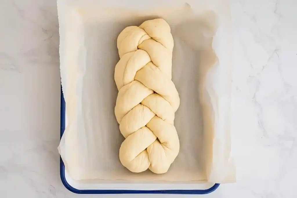 A freshly braided sourdough challah loaf resting on a parchment-lined baking tray, ready for the final proof.