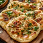 Grilled sourdough discard flatbread topped with melted cheese and sprinkled with fresh herbs.