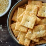 Golden, crispy sourdough discard Cheez Its sprinkled with sea salt in a bowl, with shredded cheese in the background.