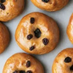 Top-down view of glossy sourdough cinnamon raisin bagels with raisins on a parchment-lined surface