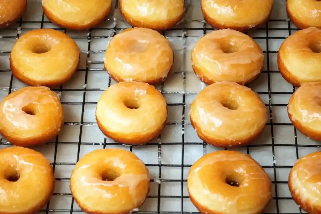 Freshly fried sourdough donuts with a shiny sugar glaze, cooling on a wire rack.