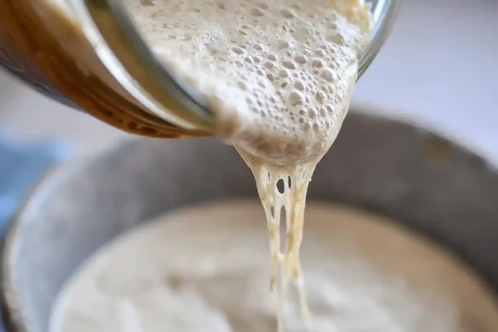 Active sourdough starter being poured from a jar, showcasing its bubbly and elastic texture.