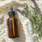 A rustic flat-lay featuring an amber glass spray bottle and fresh rosemary sprigs on a textured cloth.