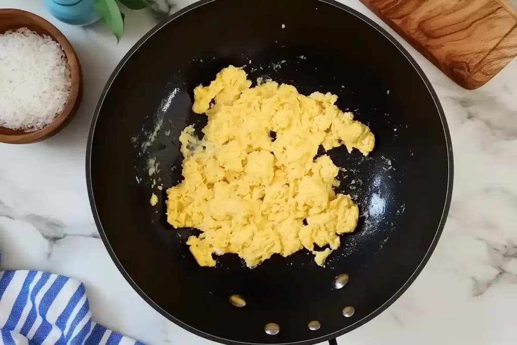 A wok with fluffy scrambled eggs cooked to perfection, ready to be mixed with rice and vegetables.