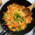 A vibrant wok filled with Anjappar Egg Fried Rice, garnished with spring onions and loaded with colorful carrots and bell peppers